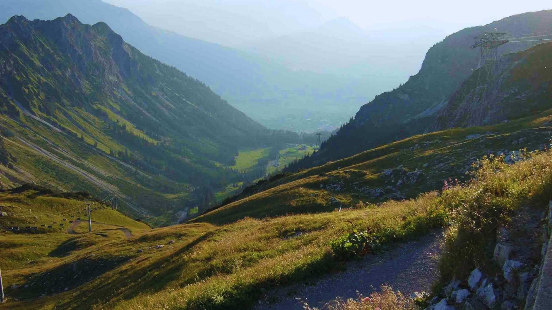 Blick auf einen sonnigen Bergpfad, der durch ein grünes Tal führt – Symbol für den lösungsorientierten Weg und die Überwindung von Herausforderungen.